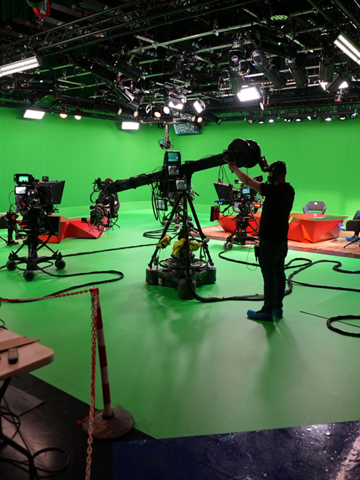 Film studio with green screen, professional lighting, cameras, and a crew member adjusting equipment.