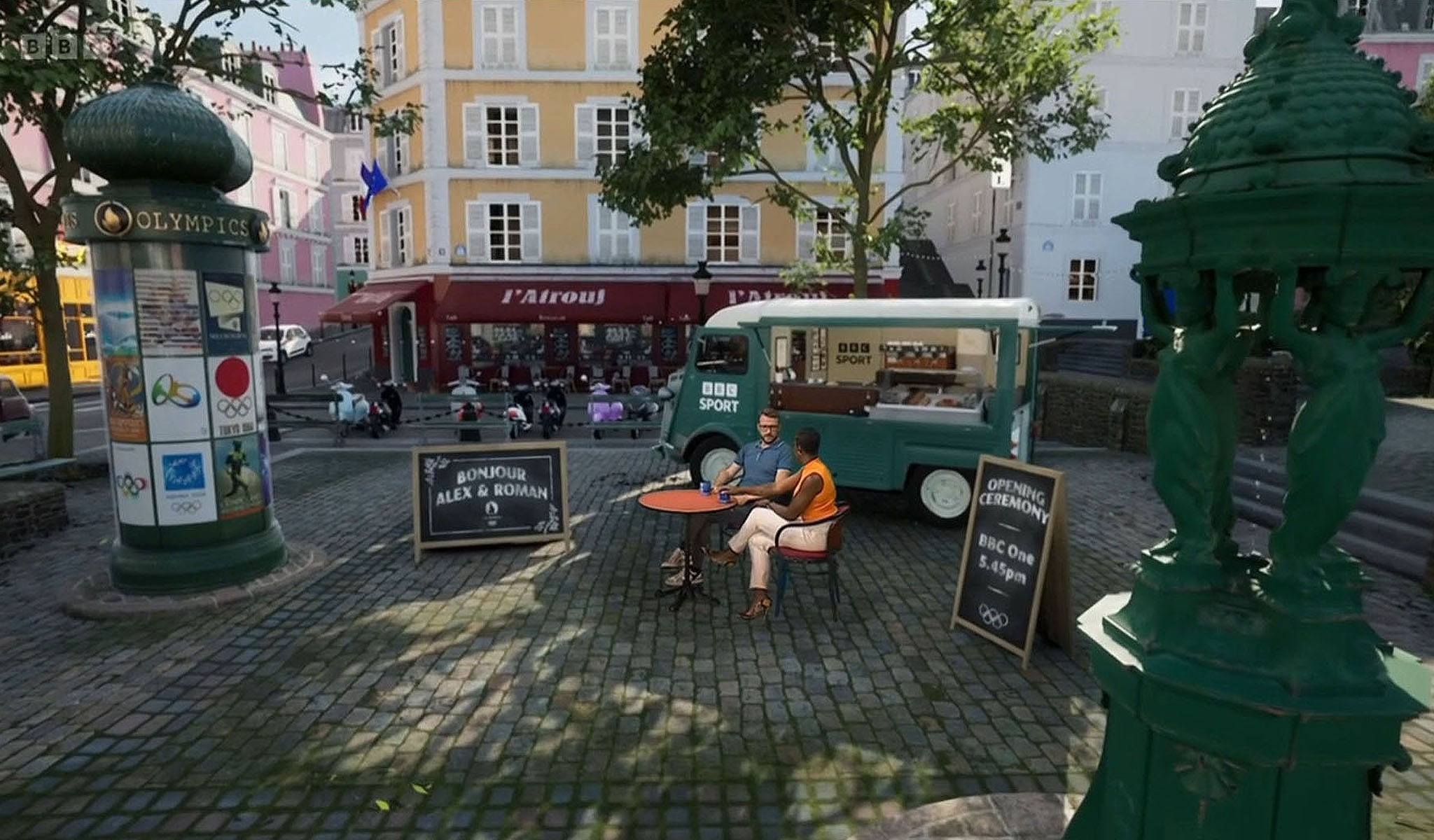 Two people sit at a round table outside with BBC Sport van and Olympic signage in a European square.