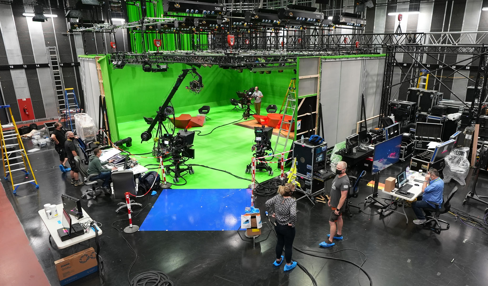 Film crew working in a large green screen studio with cameras, equipment, and monitors.