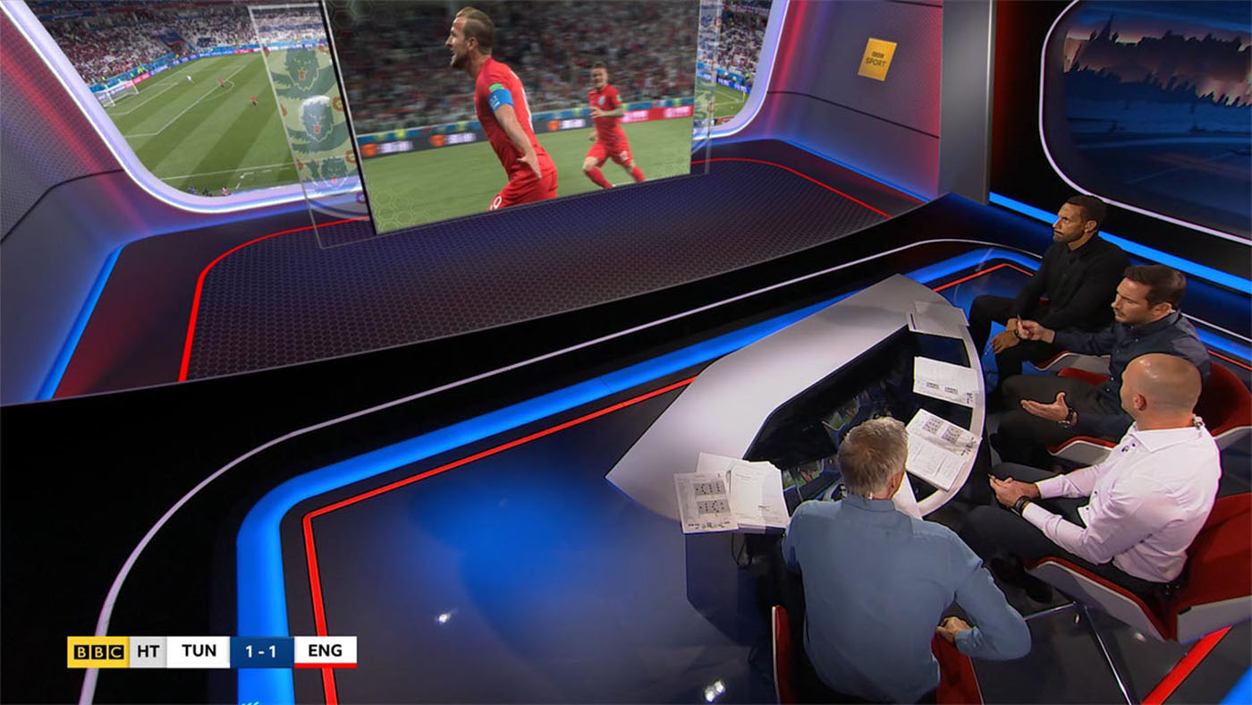 This view is from a high camera, fixed to a rail above the presenters heads. Although half of this scene is virtual, no greenscreen was required, as the set was carefully planned to make effective use of masking. In the virtual section, we see a video window displaying the FIFA UHD feed from the stadium