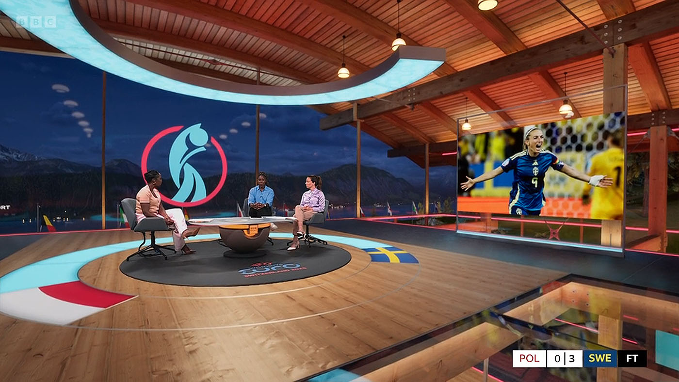 A low angled shot of Jeanette Kwakye and guests inside the BBC Sport virtual set for Sweden v Poland at Euro 2025. A lareg screen displays Swedens Asllani celebrating scoring a goal.