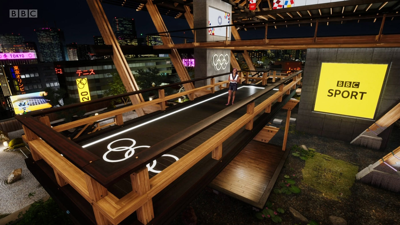 Presenter Alex Scott walks towards camera, along a timber platform within the virtual pavilion designed for BBC. Below the platform is pool in which irtual koi carp can be seen swimming.