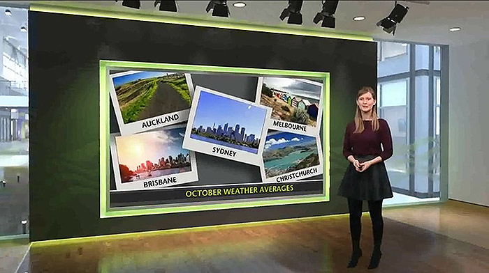 A female Met Office meteorologist presents a weather forecast using the virtual set prepared by lightwell. The virtual set features a large screen, with a wide, black surround. The waves of the m. In the background we can see the re-created interior of the Met Office HMet Office logo are embossed onto the black border. 
