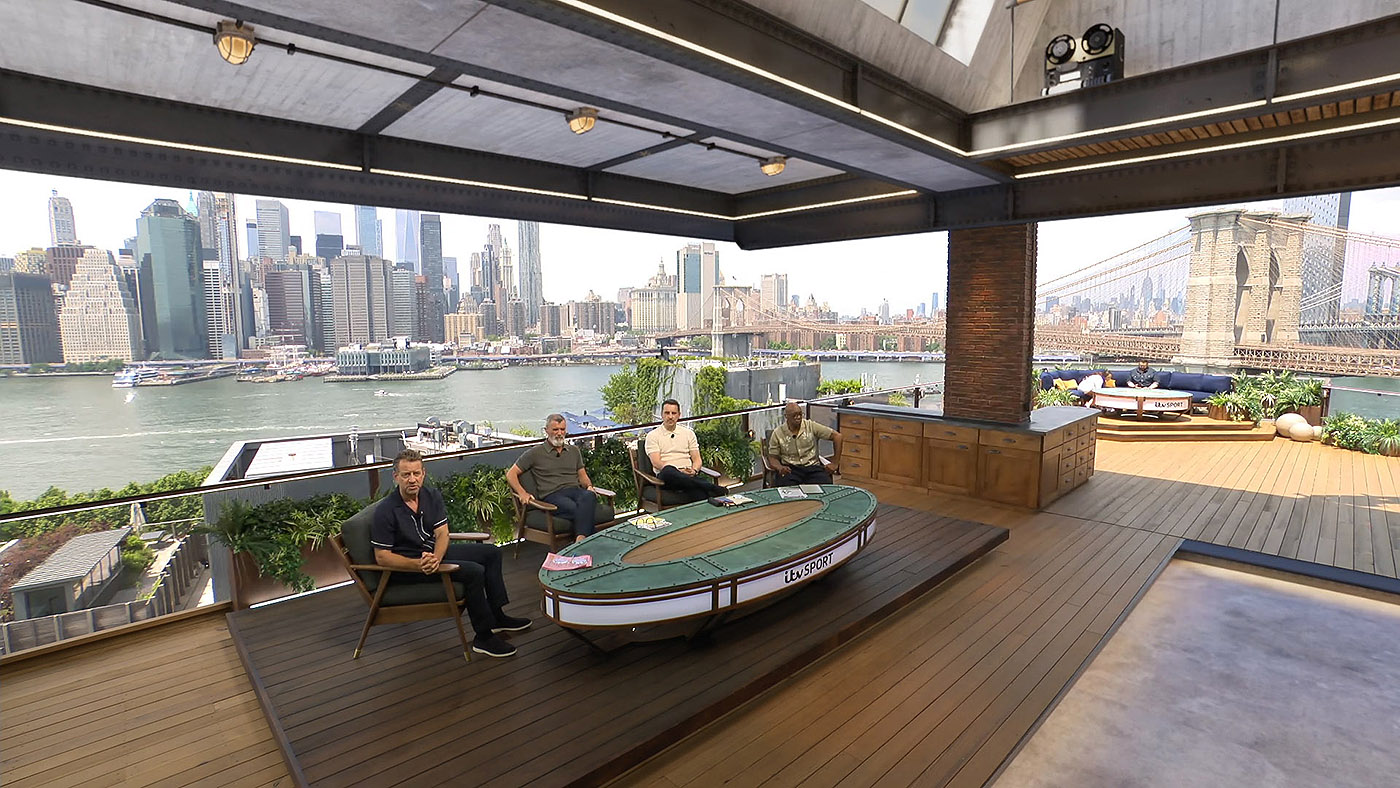 A wide view of the main set, showing Mark Pougach the main presenter with pudits Roy Kean, Gary Neville and Ian Wright seated to his right. Above is the virtual ceiling which frames views of Manhattan and the Broooklyn Bridge in the background.
