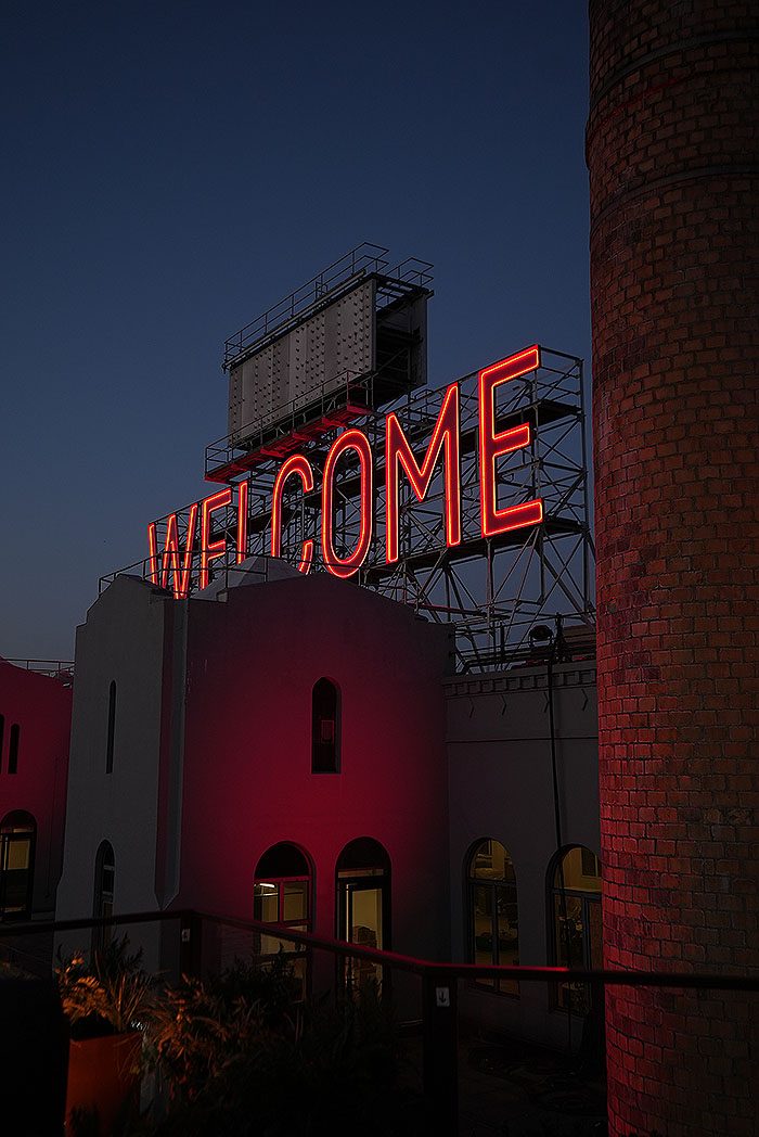 A night shot showing the neon sign reading "WELCOME" which sits above the set.