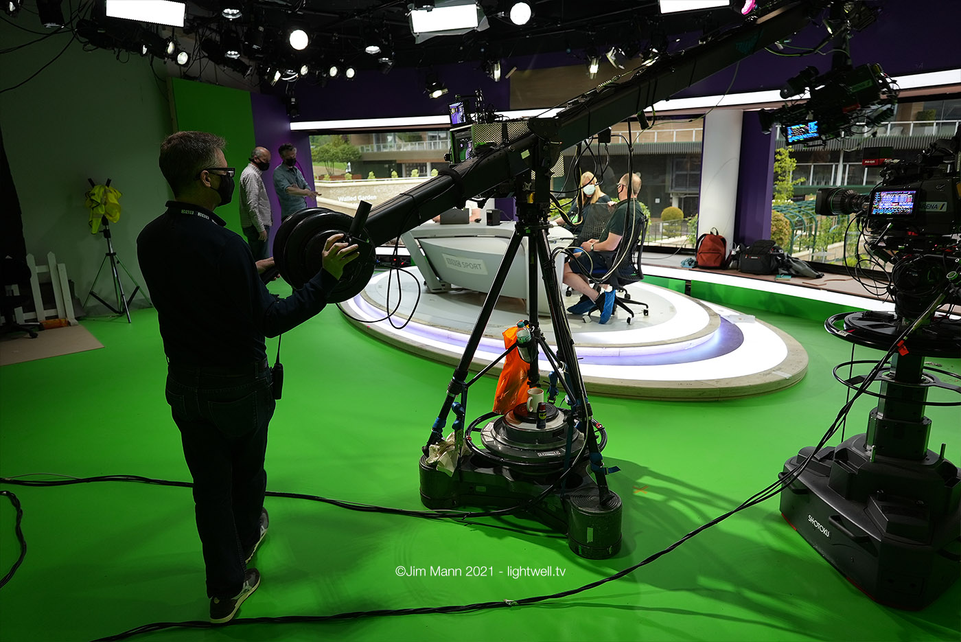 Carl the cameraman operates the jib mounted camera from the back of the Wimbledon studio. two monitors are visible on the camera pedestal - one shows the real feed, the otehr shows the phsyical studio composited together with the virtual set.
