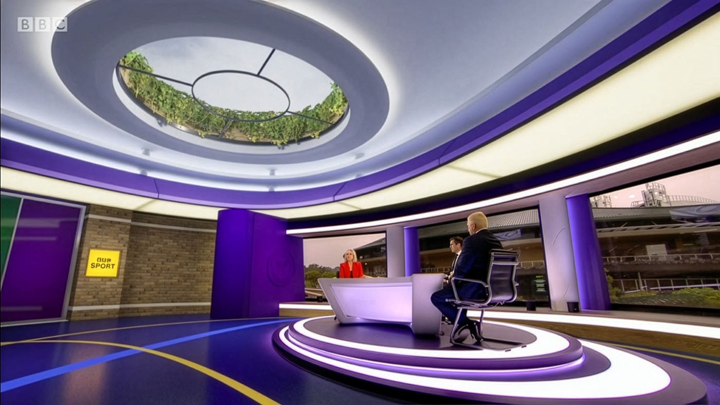 The on-air version of the set and virtual set. Sue Barker sits at the new desk design with Tim Henman and Boris Becker. In the background we can see Centre Court through the window. The rest of the set - floor, walls, ceiling and occulus dressed in ivy - is virtual.