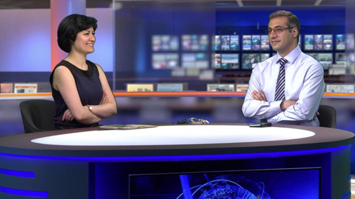 Two presenters sit at the desk. In the background, we see the virtual studio and newsroom achieved using using the Tricaster system