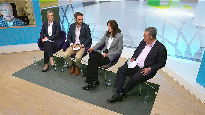 A high angle of a presenter and three guests sit inside a virtual studio designed for BP. The virtual space features a wooden floor, backed by a glass panel decorated with the frosted BP logo.