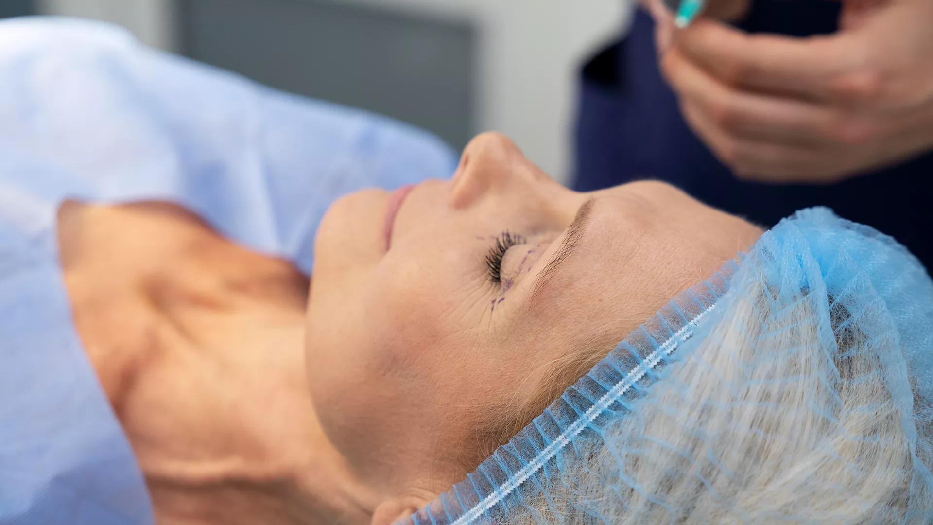 A patient lying in a clinical treatment setting while a clinician prepares for a facial procedure, with treatment markings visible around the eye area. For a Dental Examination, the key related elements are oral health assessment, tooth decay detection, gum health evaluation, oral cancer screening and personalised treatment planning, which help identify dental problems early and maintain long-term oral health.