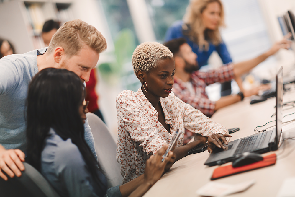 Diverse group of coworkers collaborating at computers in a modern office workspace.