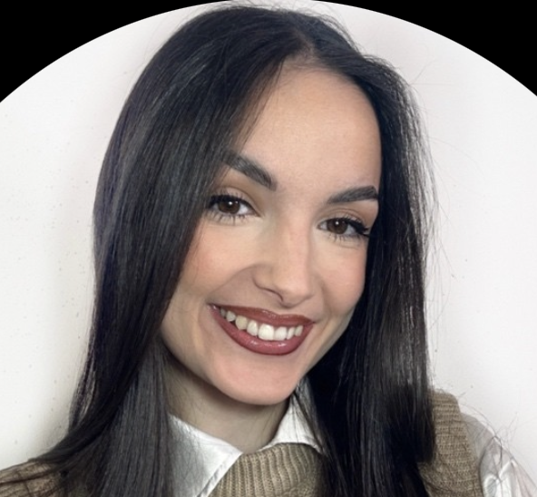 Smiling young woman with long dark hair wearing a white collared shirt and beige sweater vest.