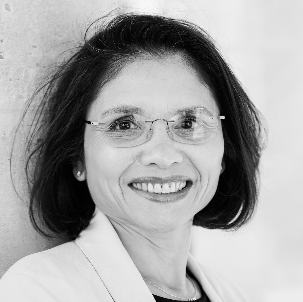 Smiling middle-aged woman with glasses and short dark hair wearing a light blazer.