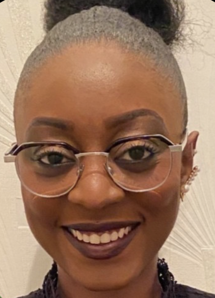 Close-up of a smiling woman with glasses, dark lipstick, and hair tied up in a bun.