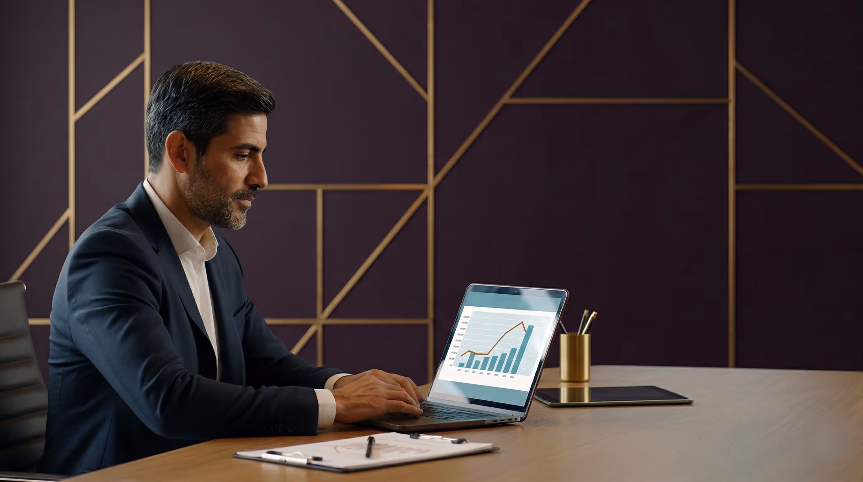 Man in business attire working on a laptop showing a rising bar and line graph in a modern office.