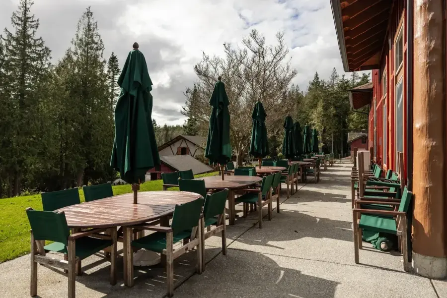 Multiple wood tables with chairs and green umbrellas on a concrete patio ready for hosting retreats and events in Skagit county.