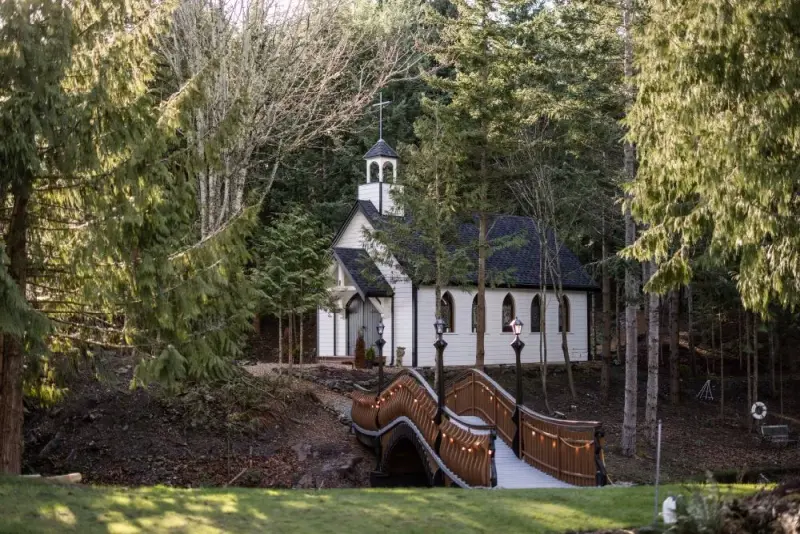 A wooden bridge goes over a pond leading to a classic white country-style chapel for weddings in Anacortes, WA.