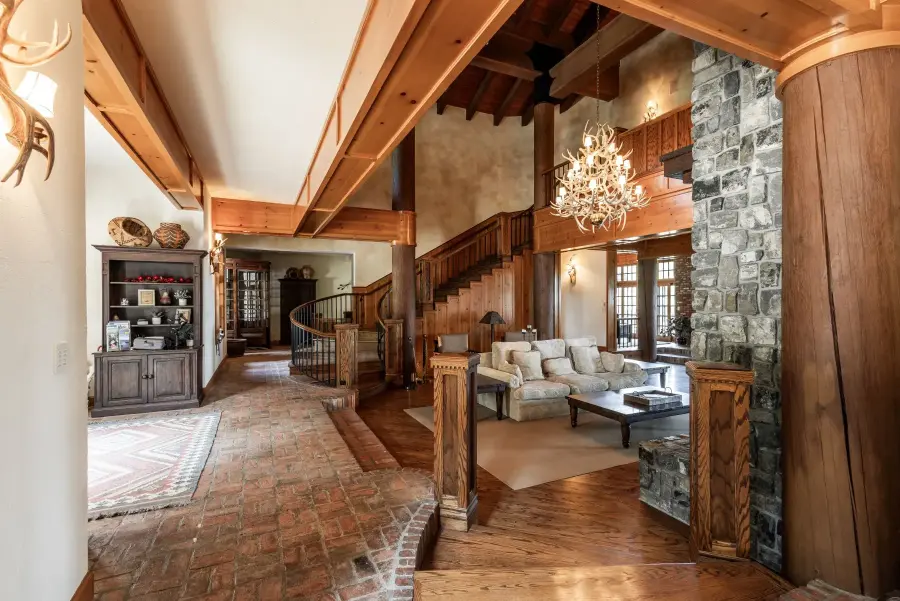 Large luxurious living room at a vacation rental in Anacortes features grand staircase, wood paneling, comfortable couches, stone fireplace.