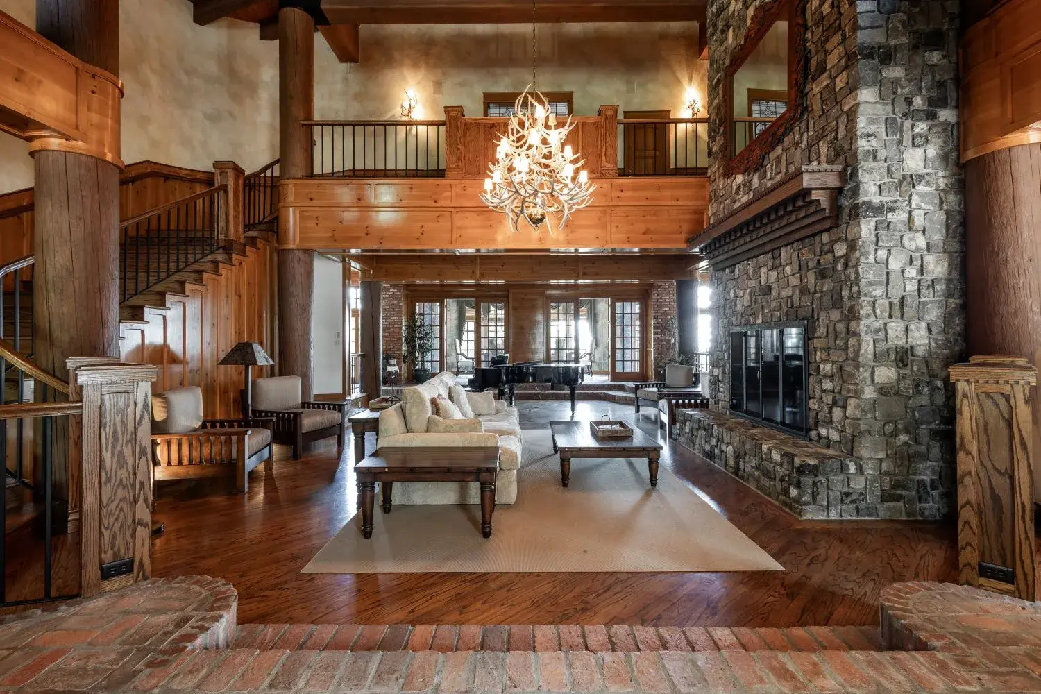 Enormous fancy living room in a luxurious wood lodge vacation rental in Anacortes, complete with chandelier, large two story fireplace, wood paneling, grand piano, and comfortable couches.