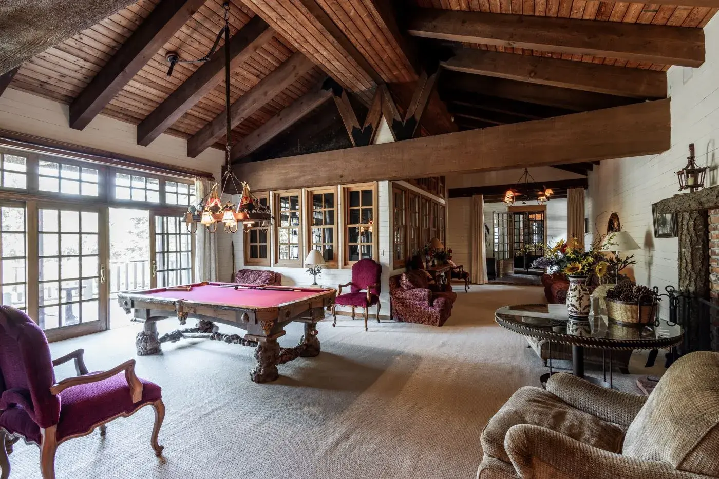 Luxury lodge recreation room with custom-made billiards / pool table, french doors, glass revolving door, chairs and couches to lounge, wood paneled ceilings and beams.