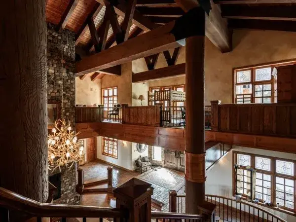 Large two story living room with wood posts, beams, ceilings, two story stone fireplace inside a luxury lodge vacation rental. 