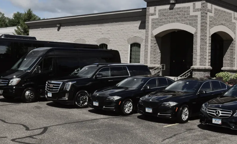 Black luxury vehicles including SUVs and sedans parked in front of a gray stone building with arched doors.