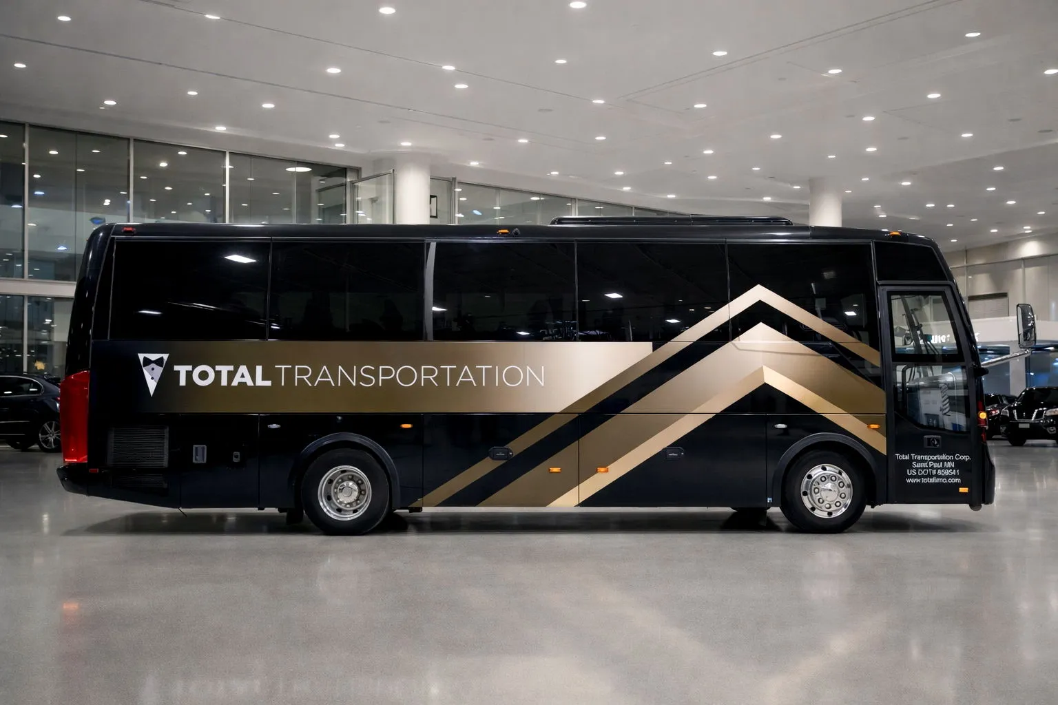 Black and gold Total Transportation bus parked inside a brightly lit building.