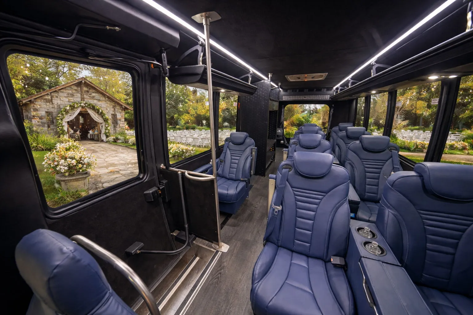 Interior of a luxury bus with blue leather seats and large windows showing a floral outdoor venue.
