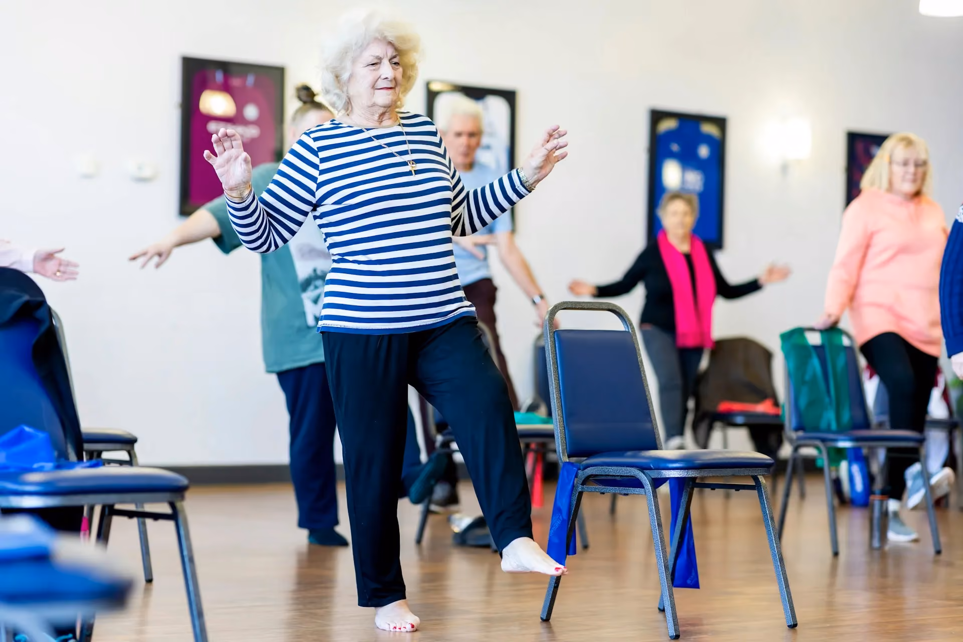 A woman in a striped shirt is dancing in a room with chairs and pictures on the walls. - Wellinks Images