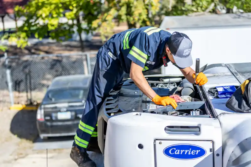 Diesel technician performing preventive maintenance on a heavy-duty truck engine, inspecting air intake and turbo components under clear blue skies.