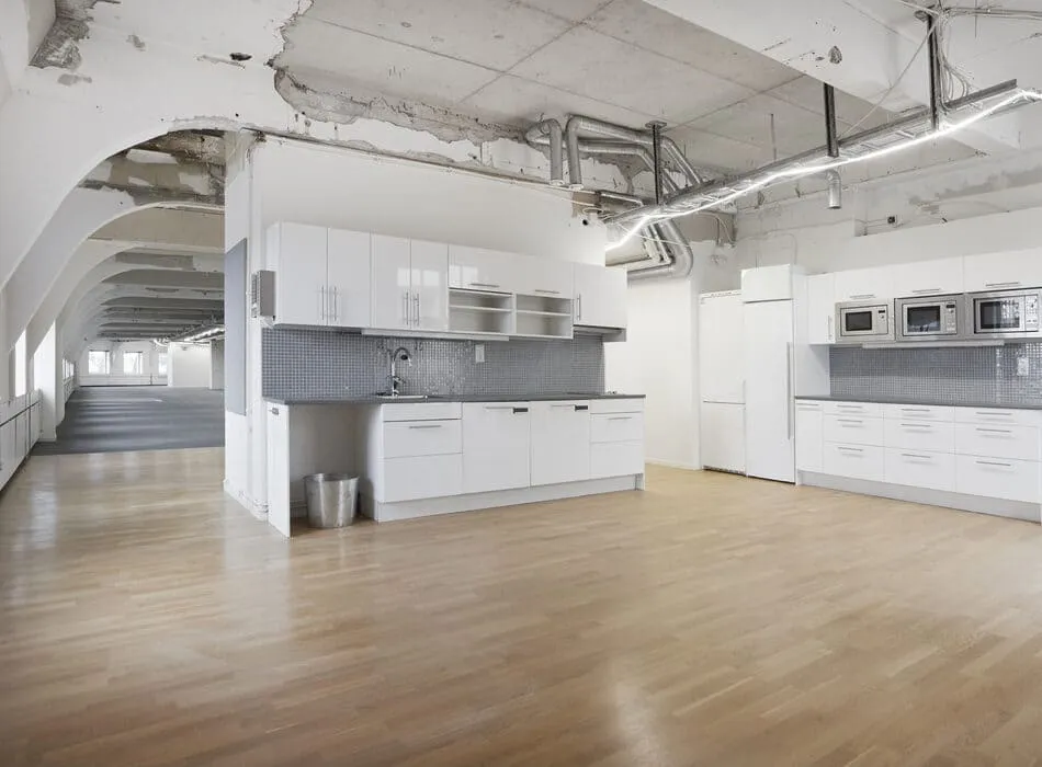 Real staging of a partially renovated commercial space with white cabinetry, exposed ceilings, and wooden flooring.