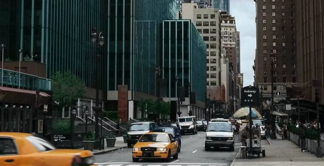 3D rendering of a busy New York street with yellow taxis and various vehicles moving past a series of modern glass buildings in Manhattan.