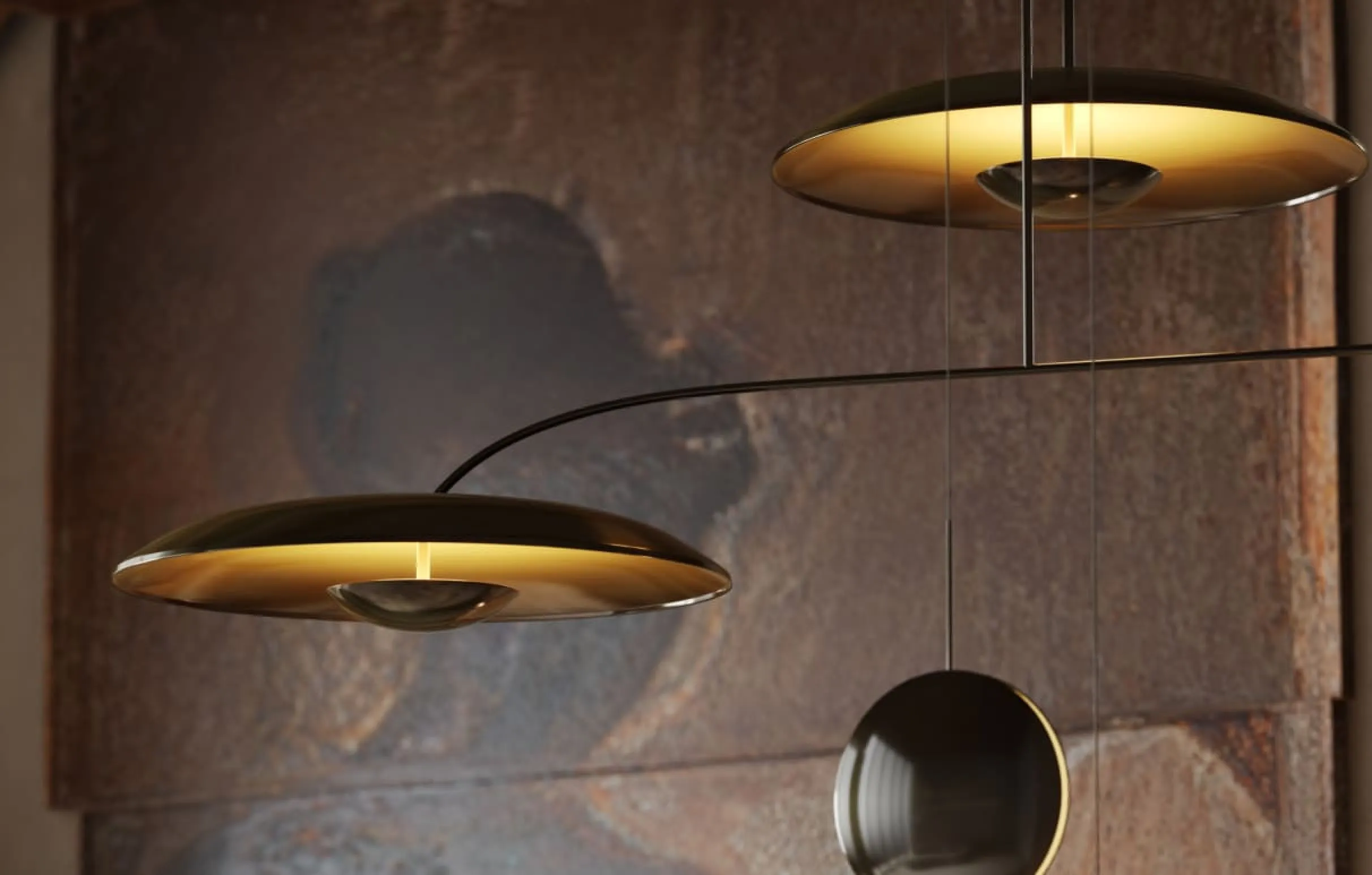 A polished 3D product rendering of a metallic pendant light with sculptural shapes, displayed against a textured stone backdrop.
