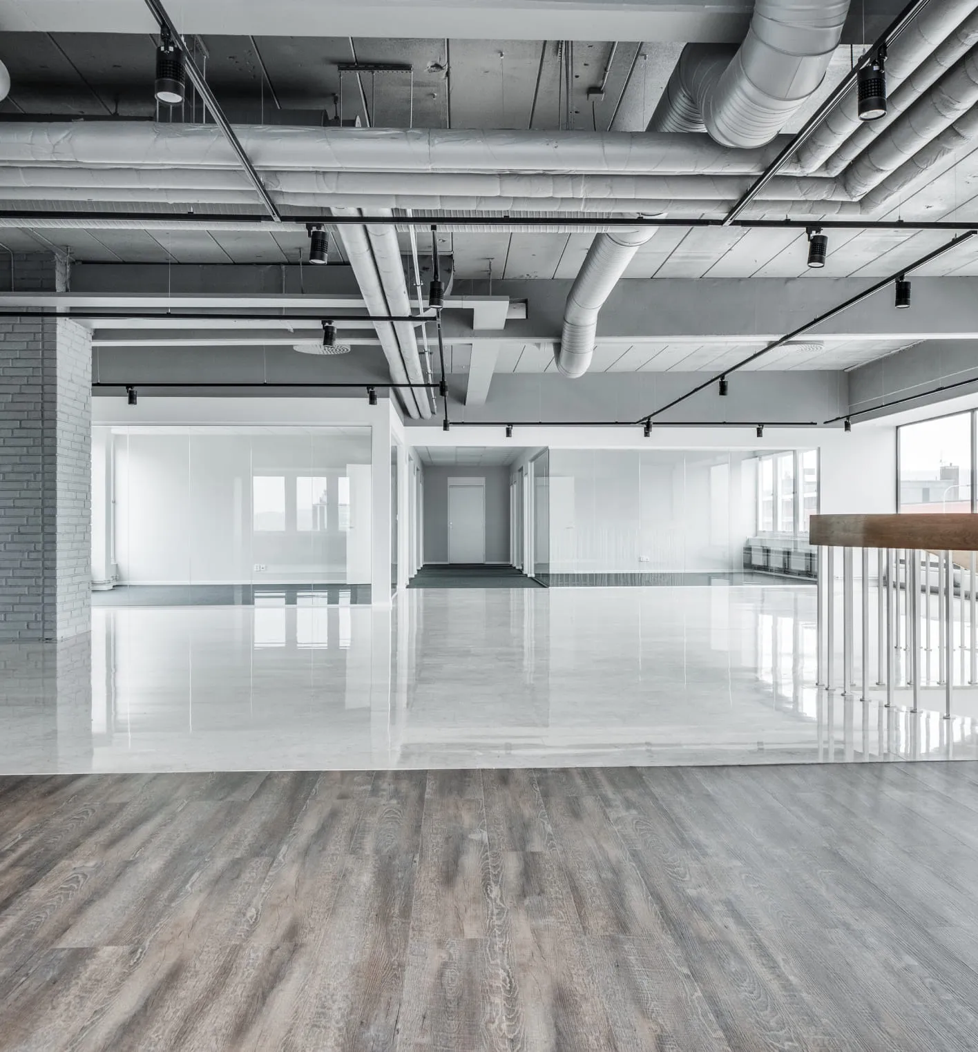 Empty open-concept property photo featuring polished concrete and wood-style floors, exposed ceiling ducts, glass partitions, and ample natural light, serving as the input material for 3D virtual staging and furniture visualization.