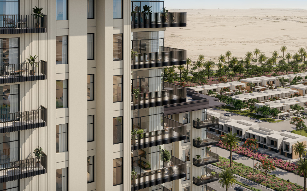 Modern desert architecture apartment complex with private balconies, overlooking a low-rise desert housing community and desert dunes beyond.