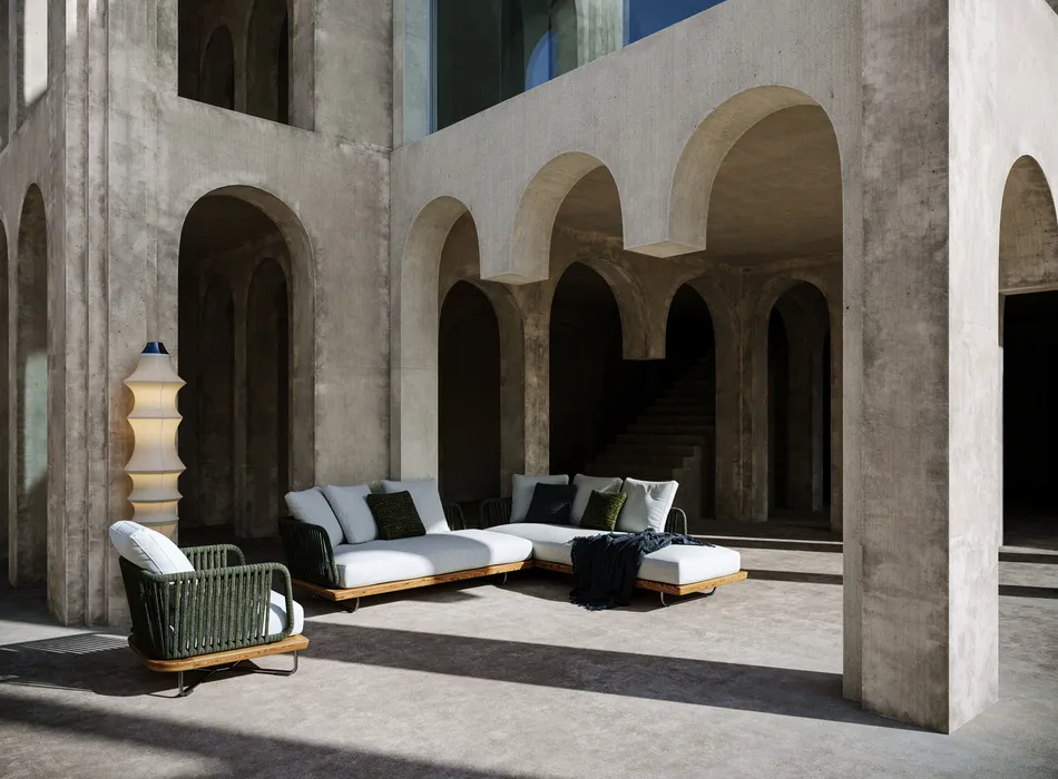 Minimalist outdoor lounge area with arched concrete architecture, showcasing outdoor furniture staging with a cushioned sofa set, armchair, and decorative lighting.