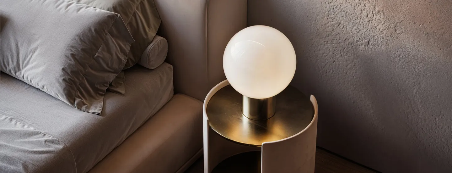 A modern luxury staging a bedroom setup with a soft neutral palette, brass globe lamp, plush bedding, and a textured wall creating a warm, serene atmosphere.