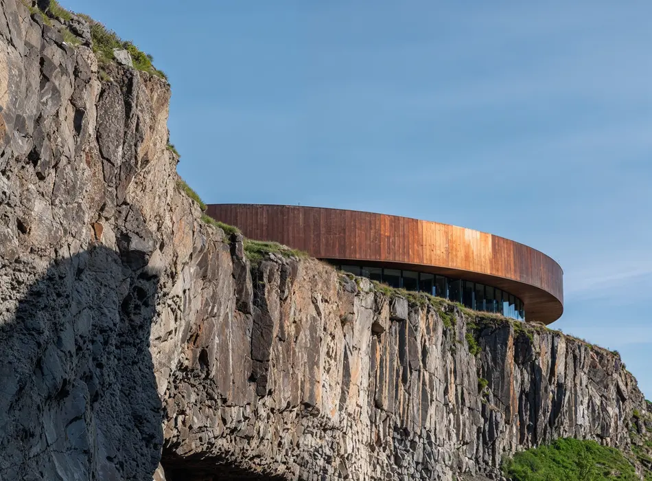 Circular cliffside building with wooden facade integrated into rocky landscape, architectural concept showing will ai replace 3d artists in environment design