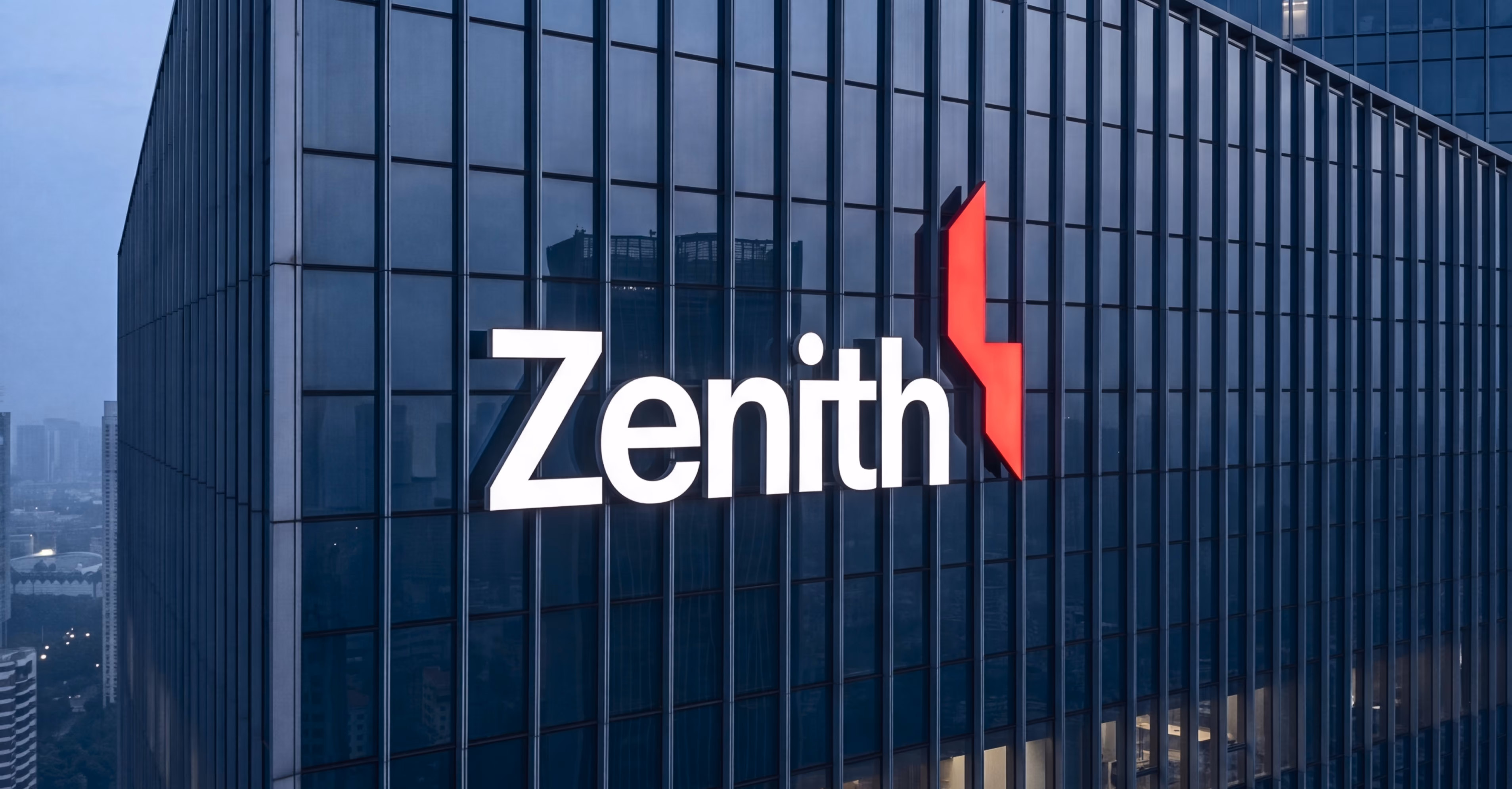 Lit Zenith sign mounted on the side of a glass skyscraper at dusk or dawn.