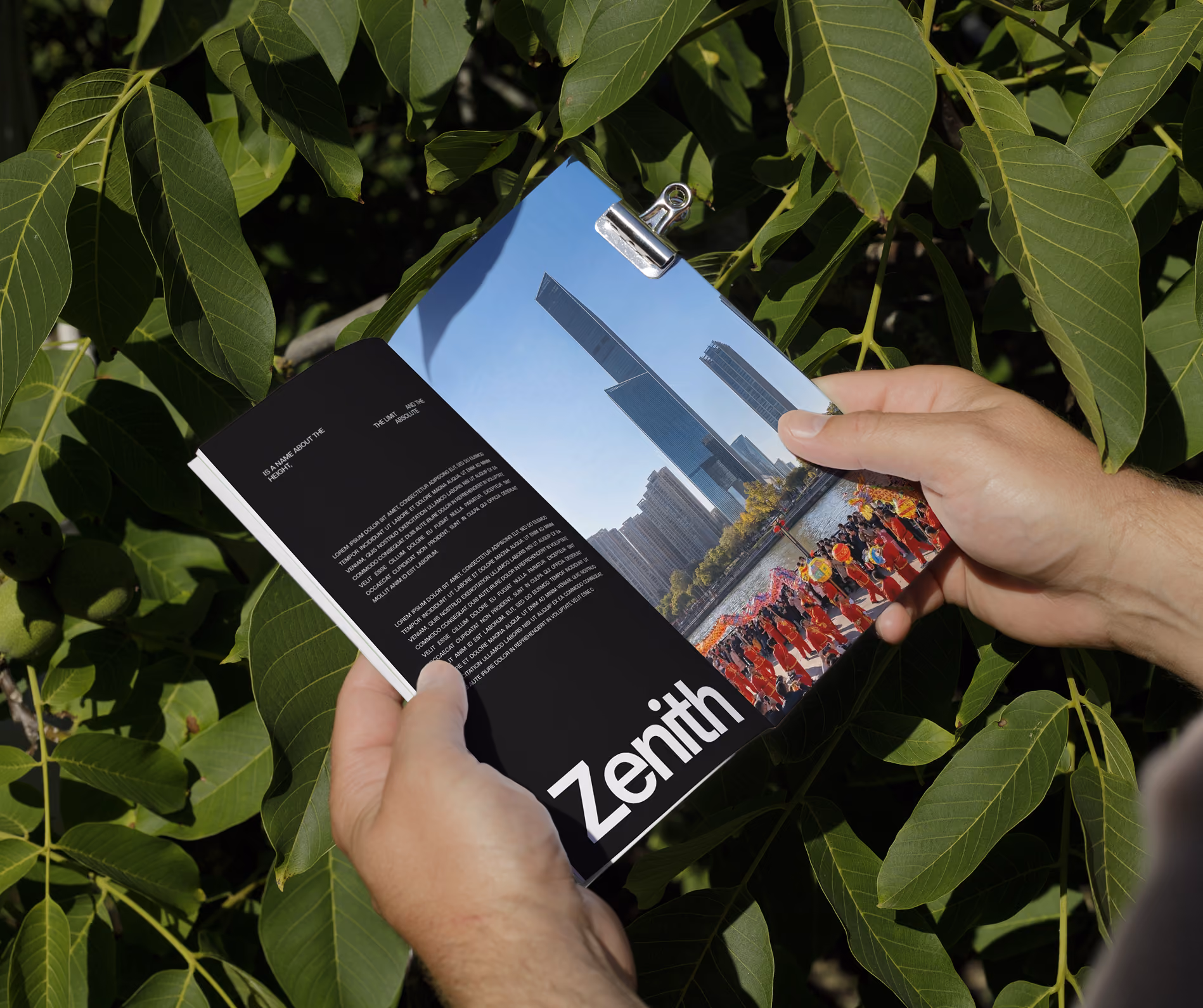 Person holding a magazine showing skyscrapers and a vibrant dragon dance event by a river.
