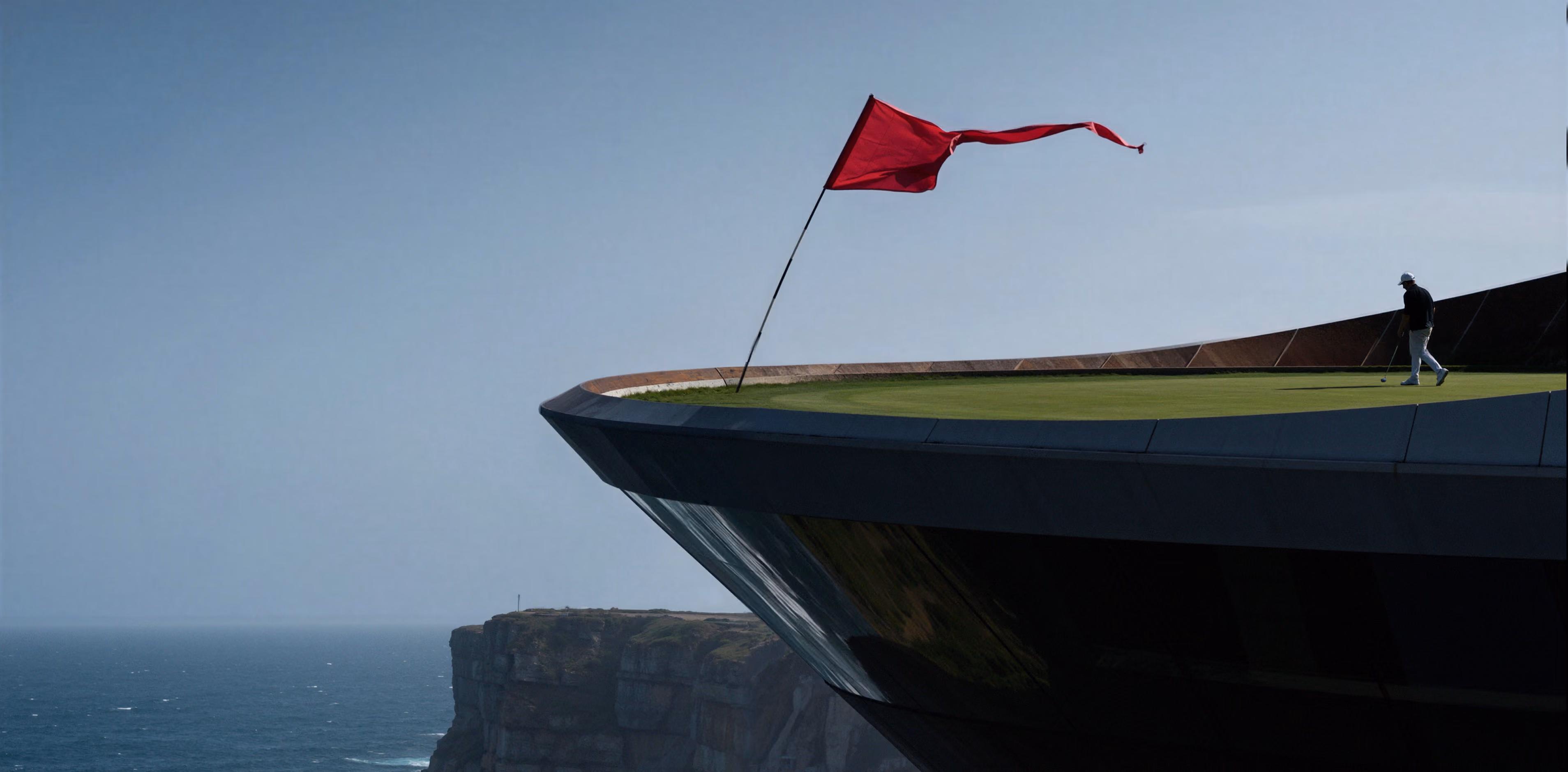 Golfer walking on a green atop a cliff-edge course with a red flag fluttering in the wind.