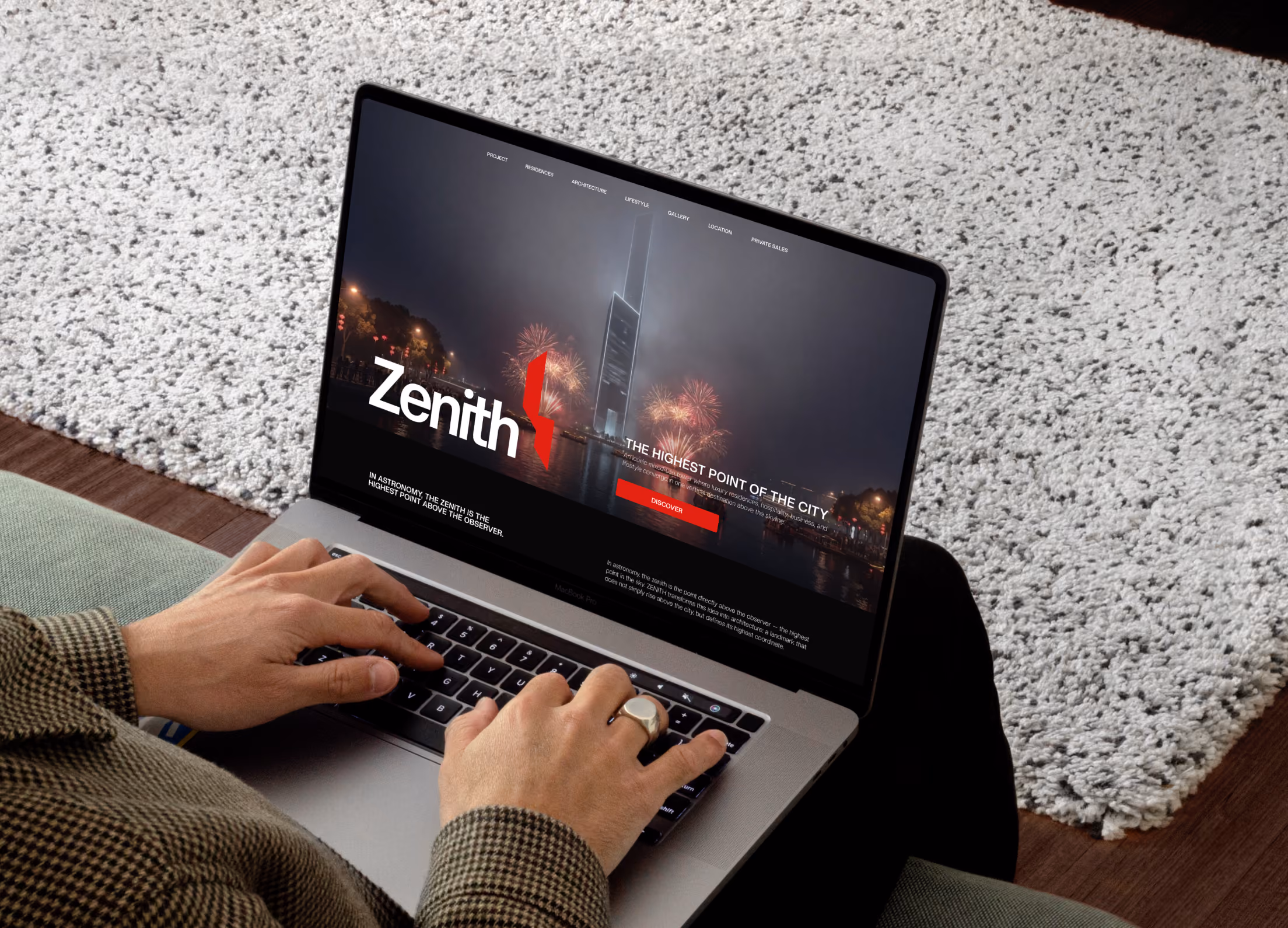 Hands typing on laptop showing webpage with 'Zenith' and fireworks around a tall city building at night.