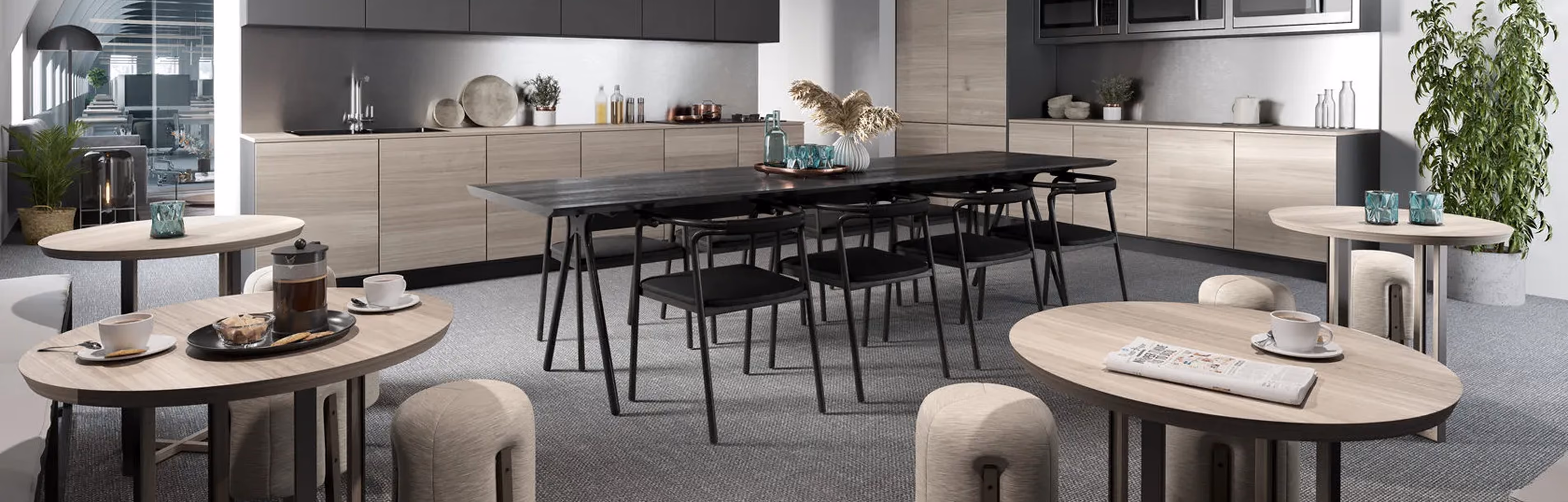 Modern office kitchen and dining area with black table, chairs, light wood cabinets, and small round tables.