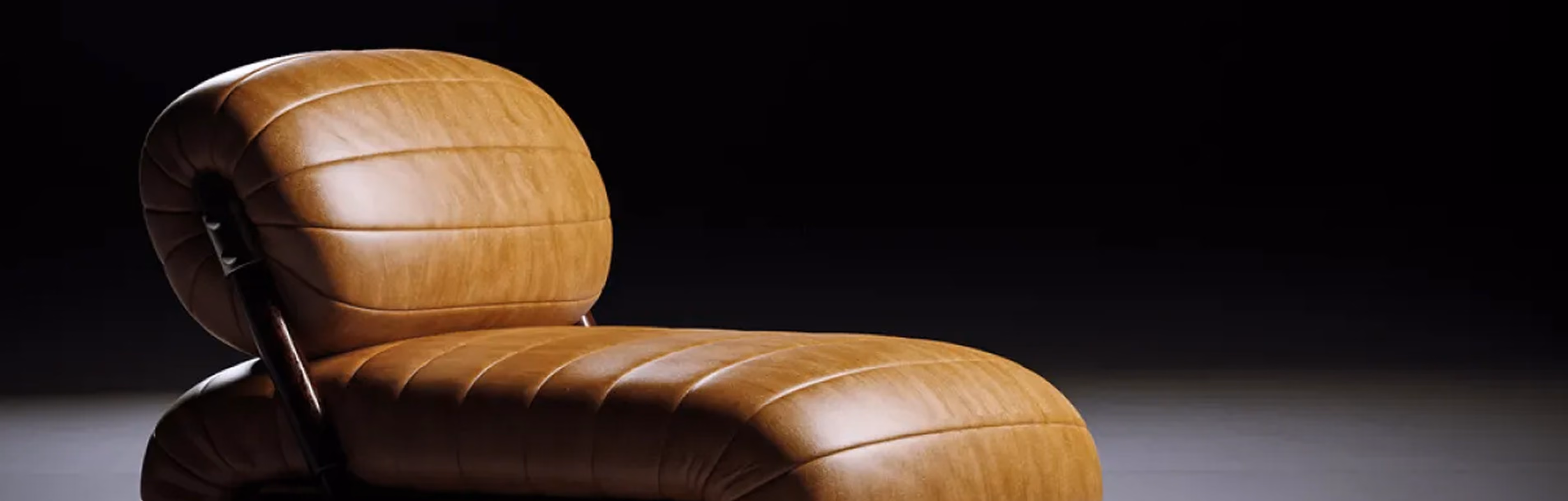 Close-up of a modern brown leather curved lounge chair against a dark background.