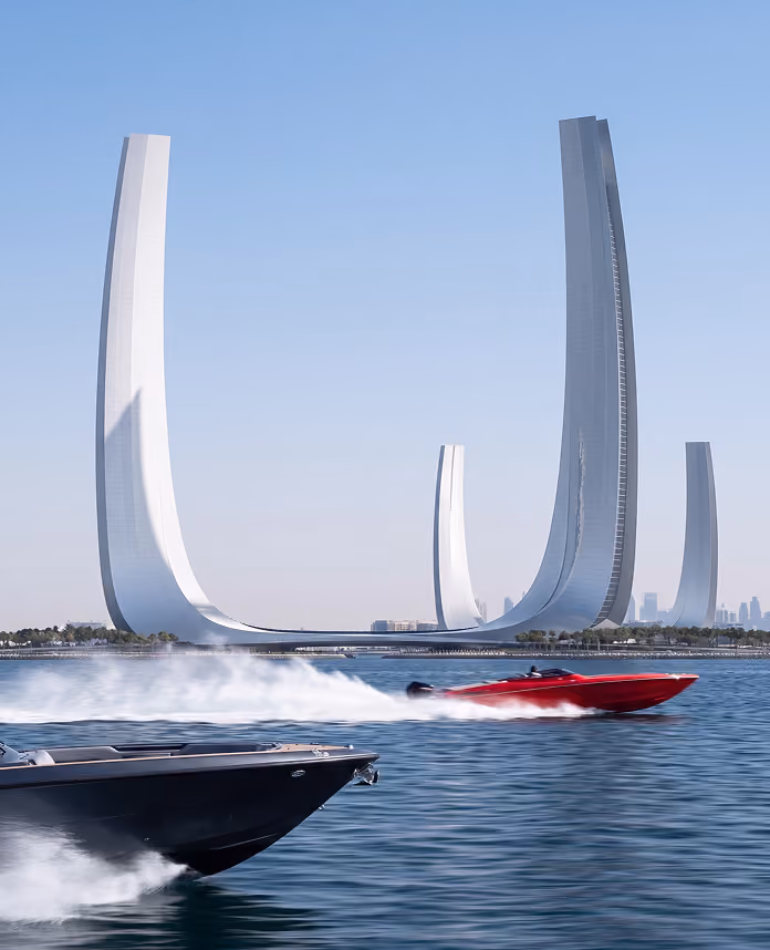 Modern architectural structure with four tall, curved, white towers arranged in a wide U shape along a waterfront, with two speedboats on the water in front, one red and one black, creating white water trails against a clear blue sky.