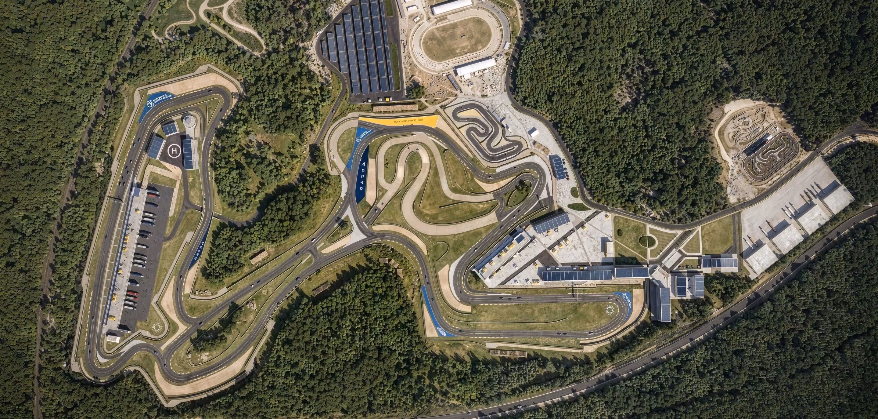 Aerial view of a modern racing circuit surrounded by dense forest, showcasing complex track layouts and support facilities — created with 3D exterior rendering services.