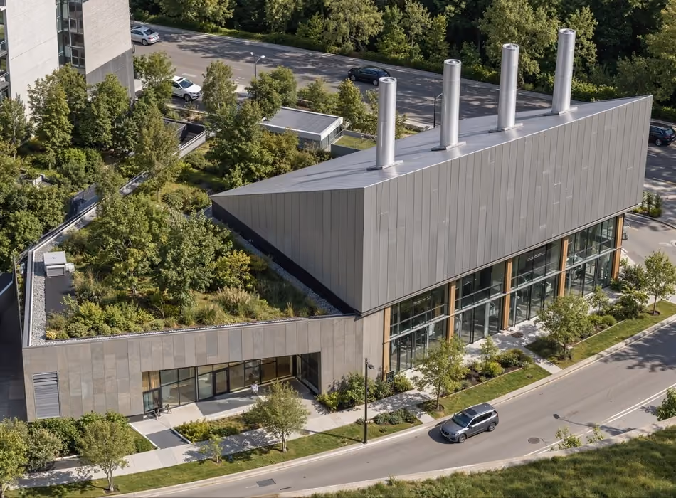 3d industrial rendering of a sustainable energy plant with angular metal cladding, rooftop exhaust stacks, green roof landscaping, and large transparent industrial facade.