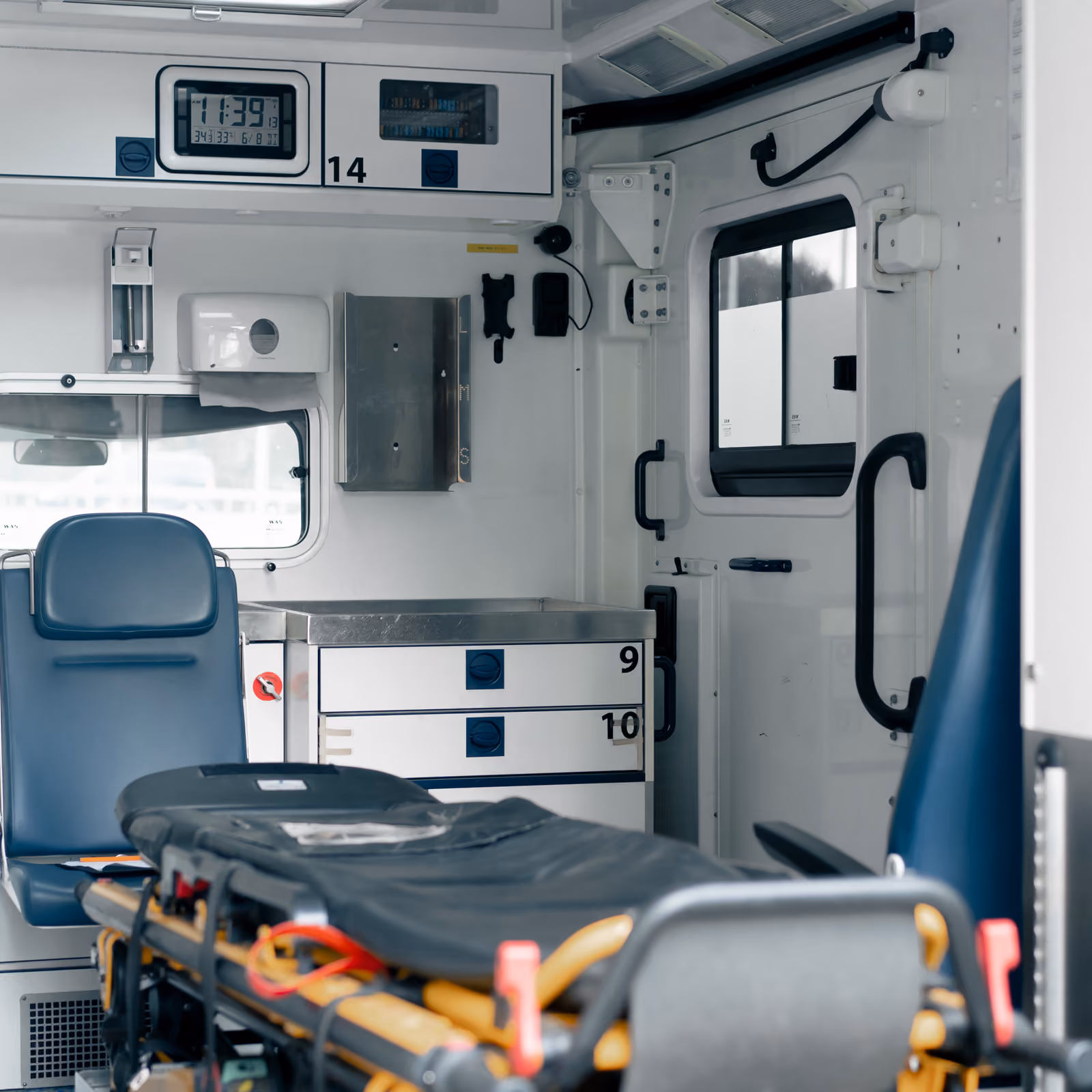 Interior of an ambulance showing stretcher, blue seats, cabinets, and medical equipment.