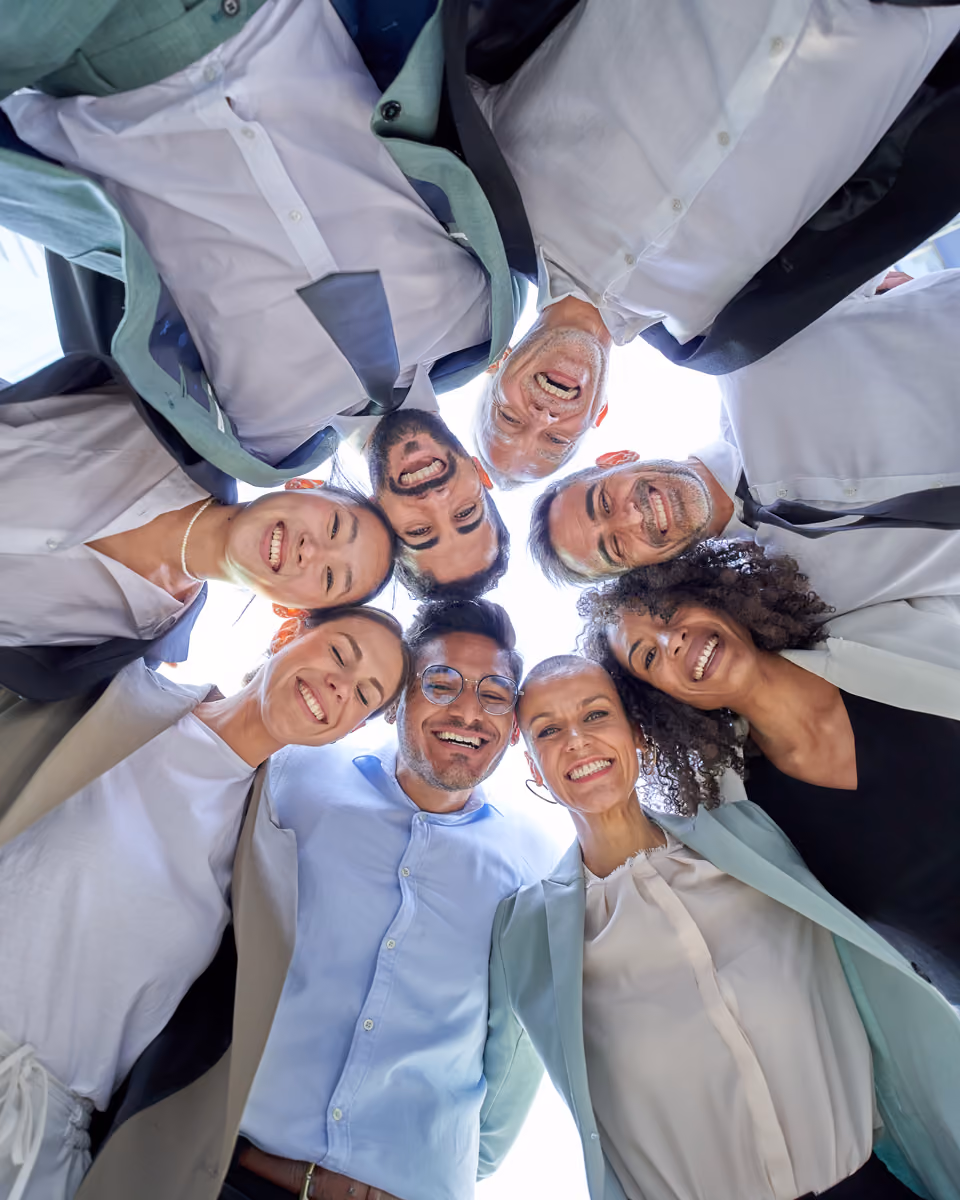 Smiling diverse professionals in business attire standing in a circle looking down at the camera.