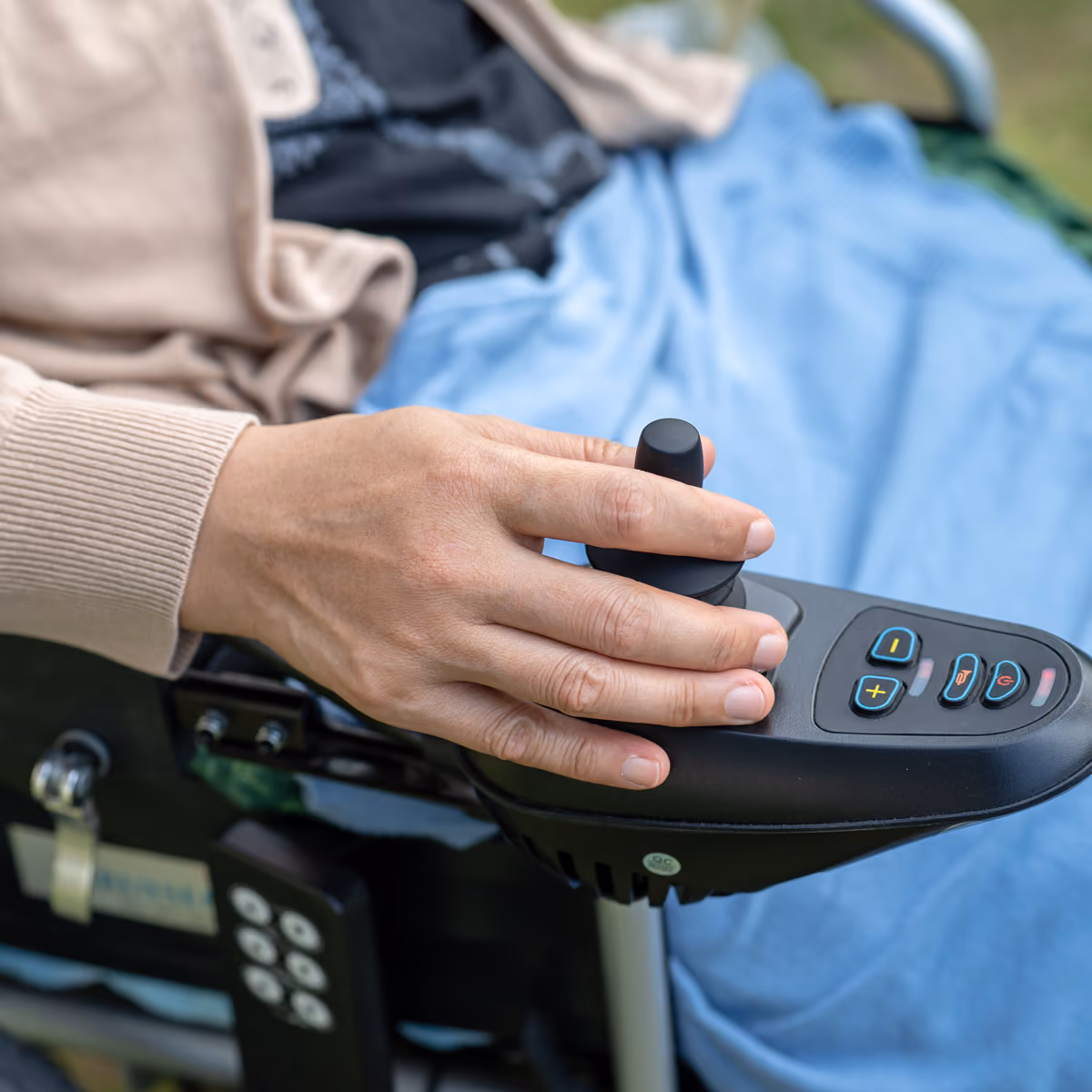 Close-up of a hand operating the joystick control on an electric wheelchair armrest.